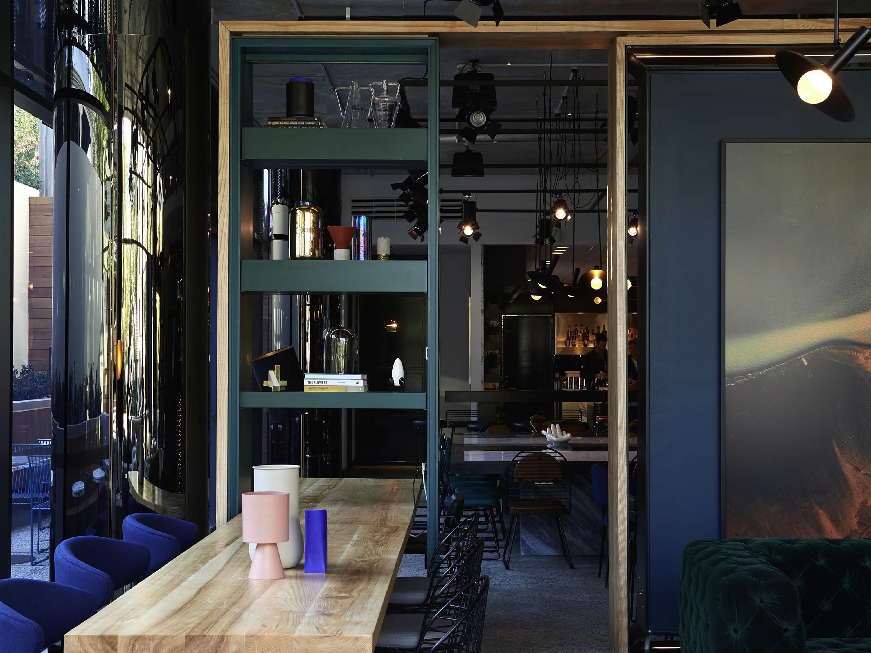 Un intérieur moderne avec une table en bois, des chaises bleues, une étagère verte et un coin bar.
