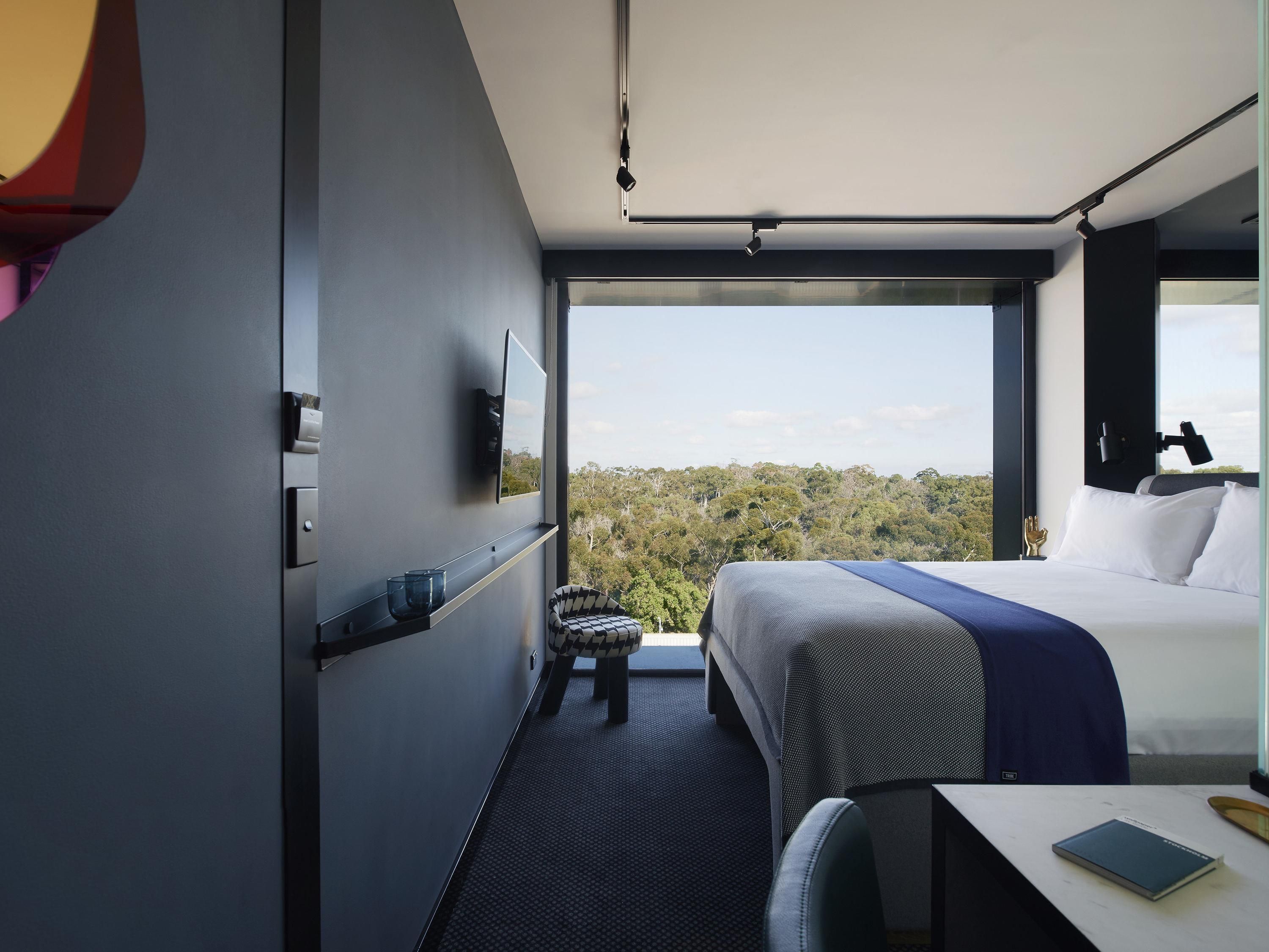 A modern hotel room with a large bed, a desk, and a view of the forest.