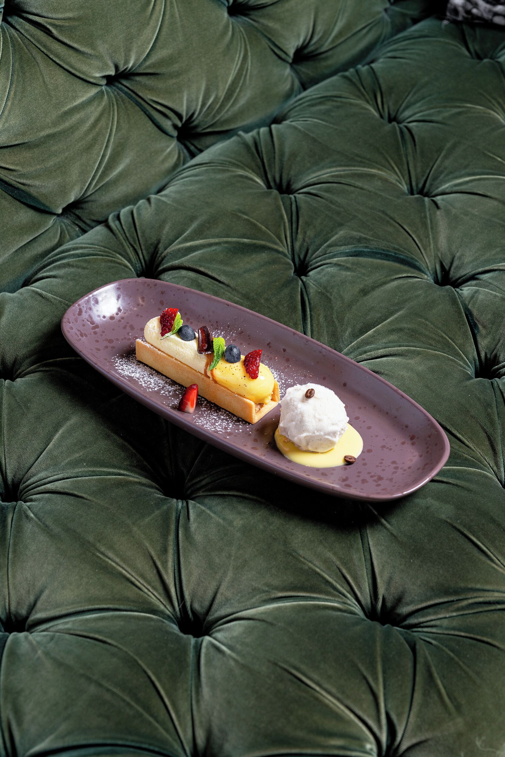 A dessert on a plate on a tufted green sofa.