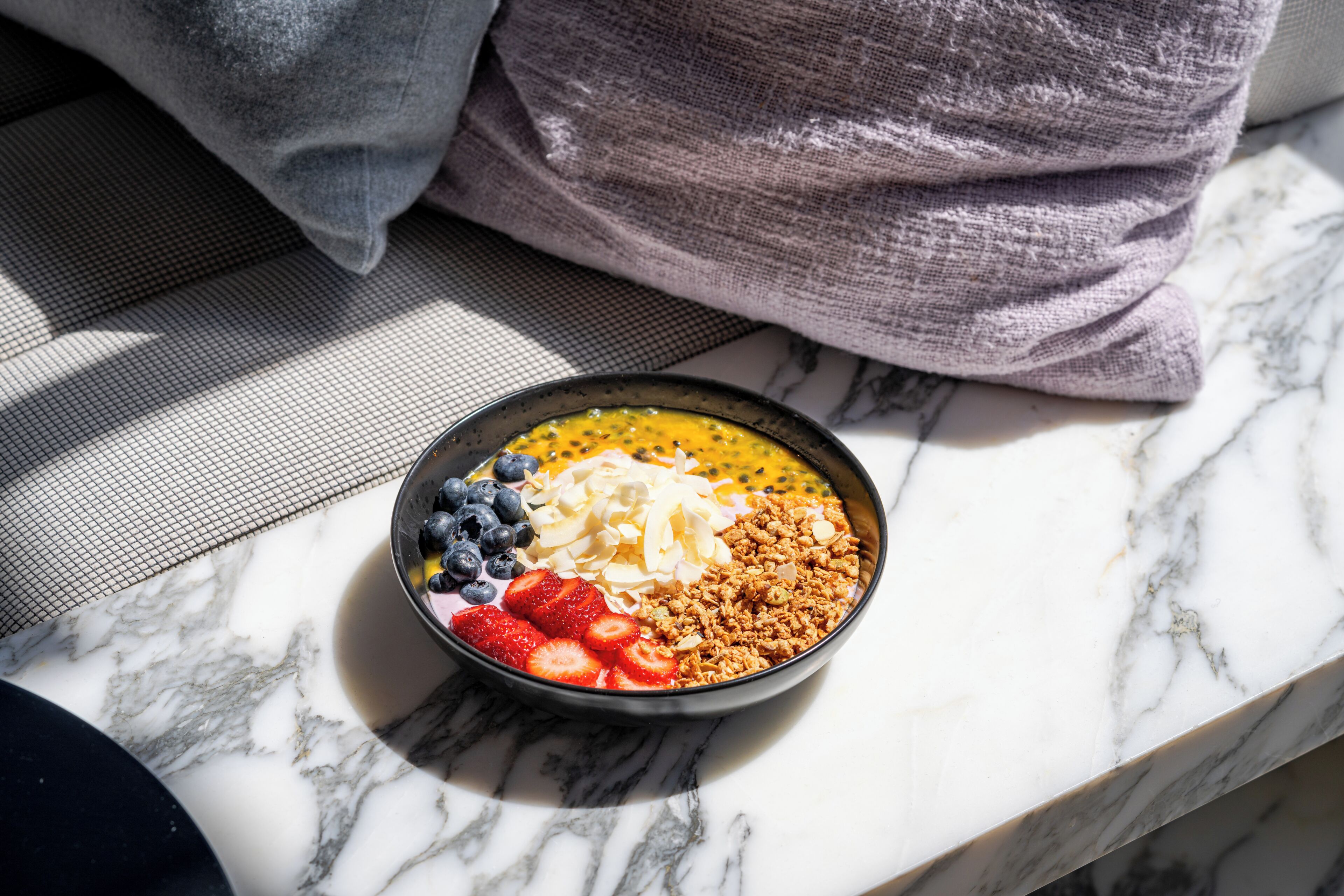 Un tazón de desayuno con frutas y granola sobre una superficie de mármol.