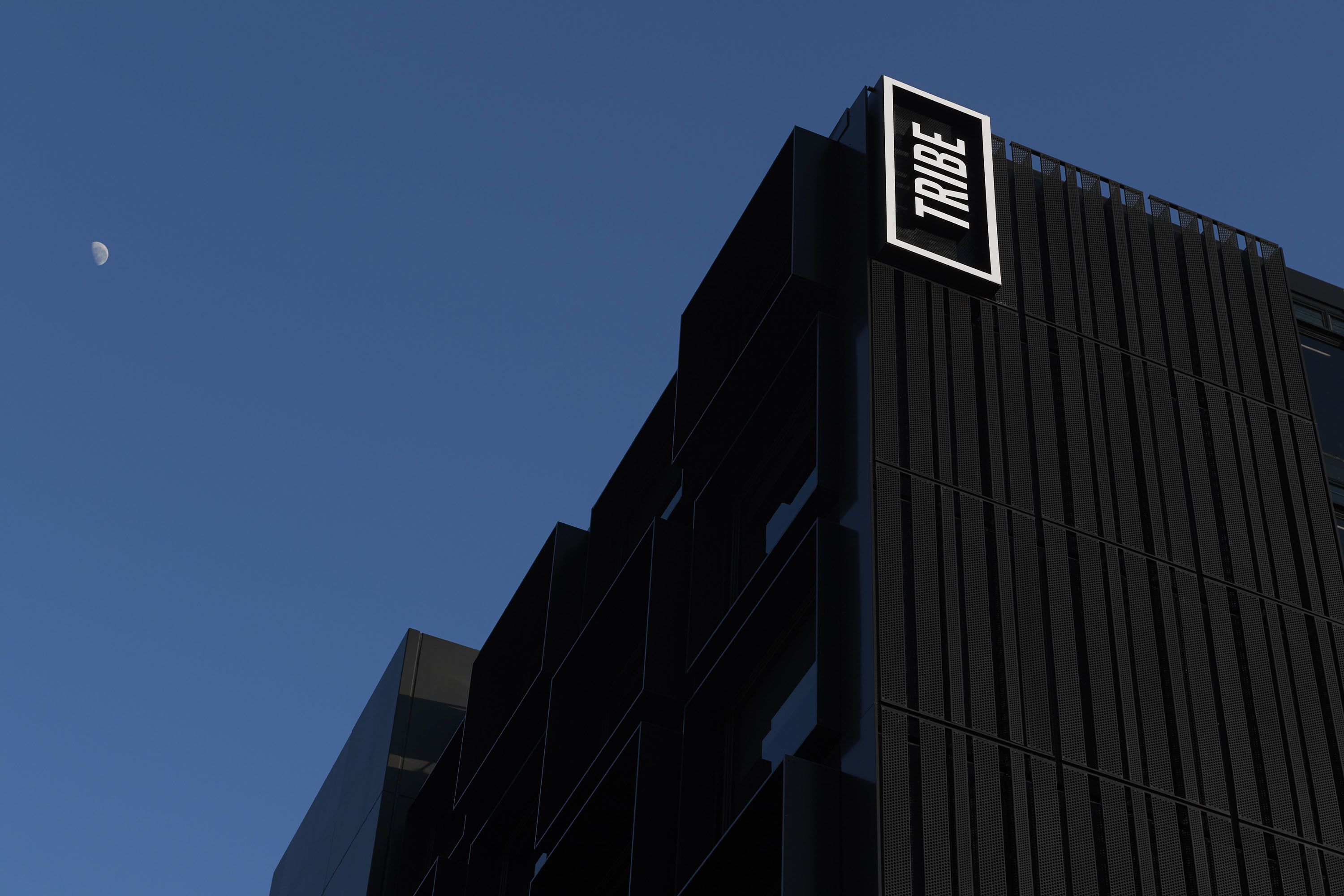 Een modern gebouw met een opvallend “TRIBE”-bord aan de zijkant.