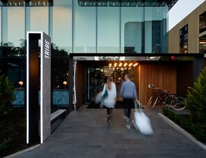 A modern building entrance with a glass facade, a sign reading "TRIBE", and a bicycle parked outside. - Tribe Perth Kings Park (West Perth)