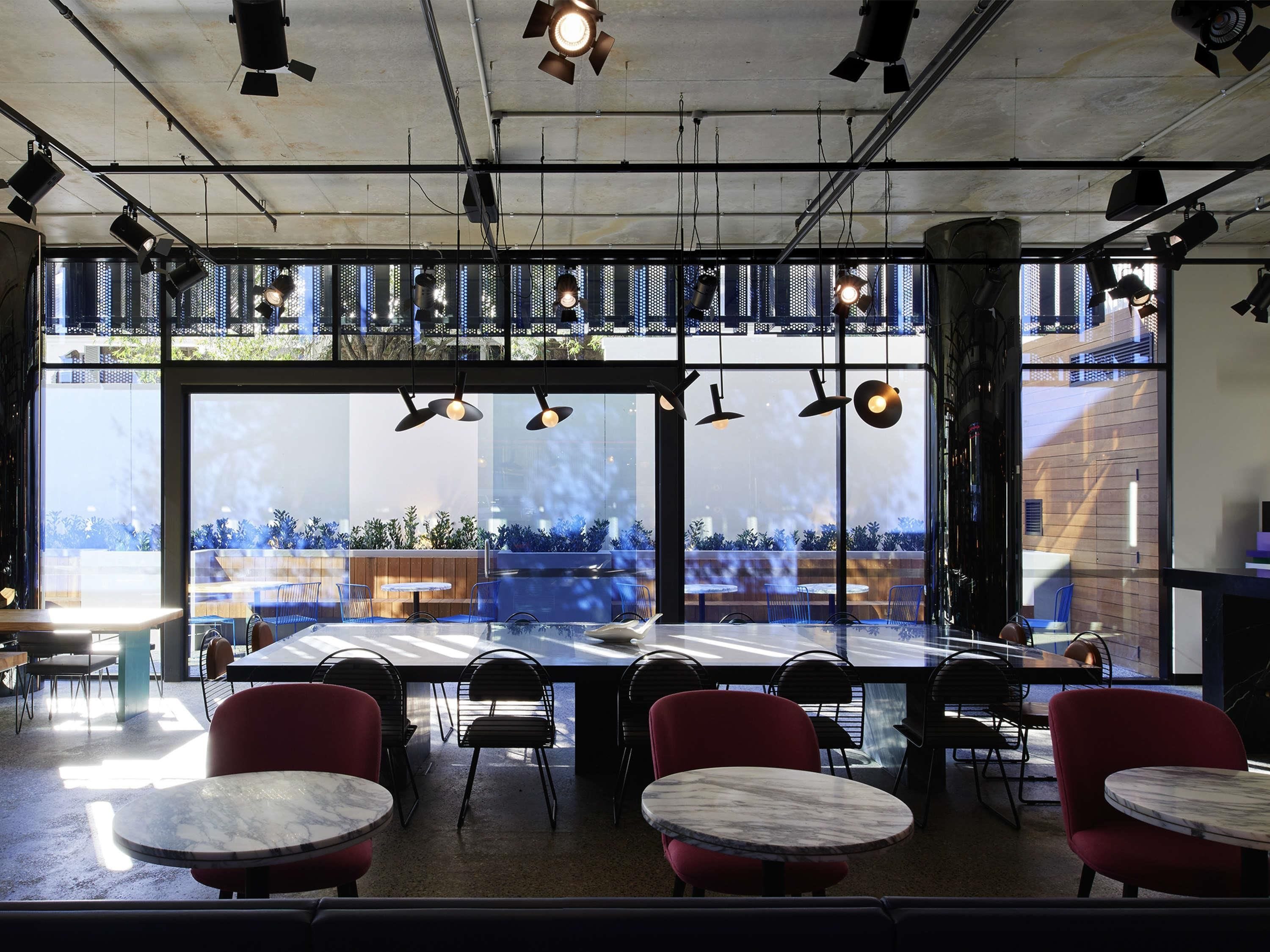 A modern dining area with large windows, multiple tables, and chairs.