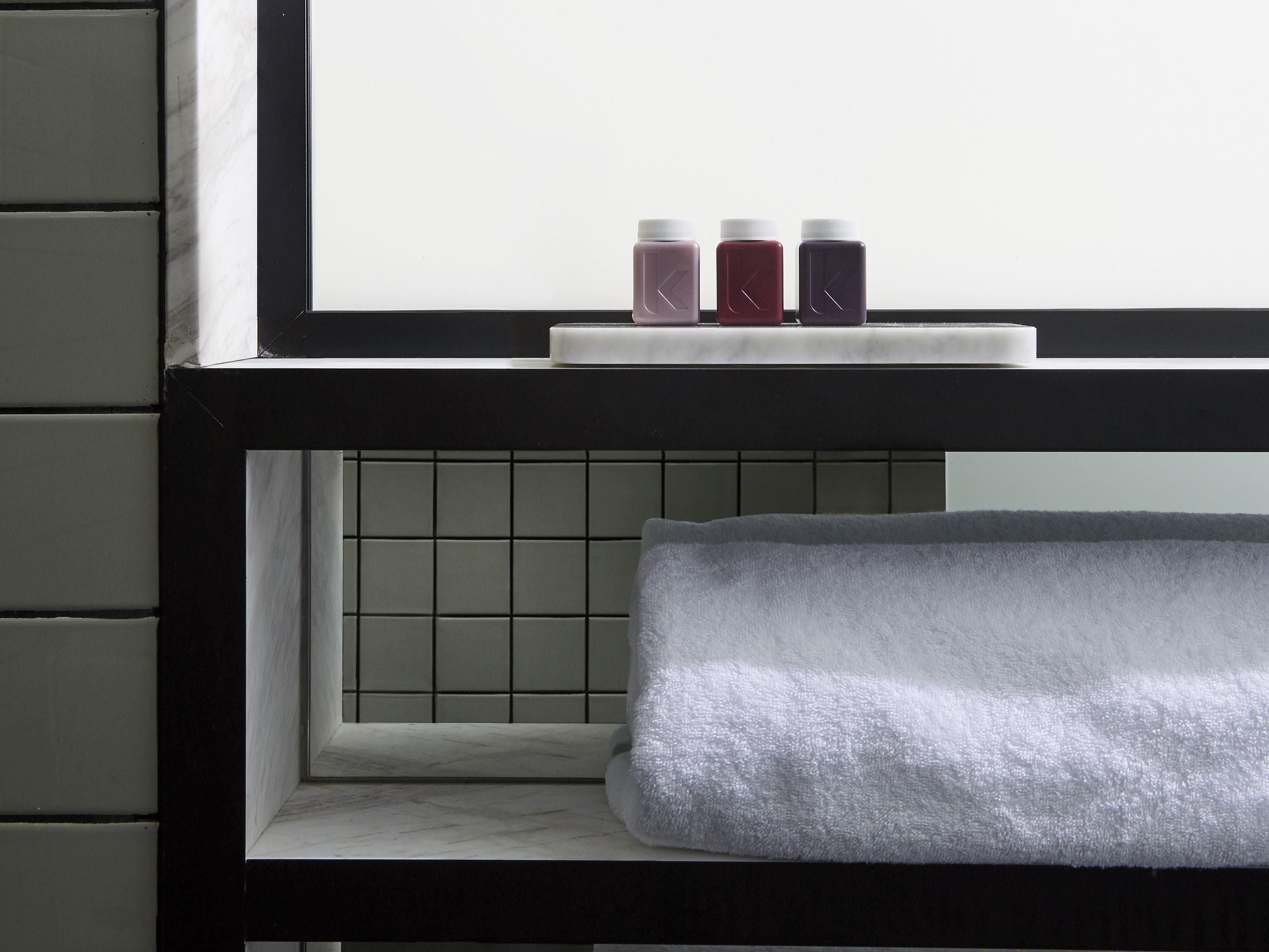 A bathroom with a window, a towel rack, and three bottles on the windowsill.