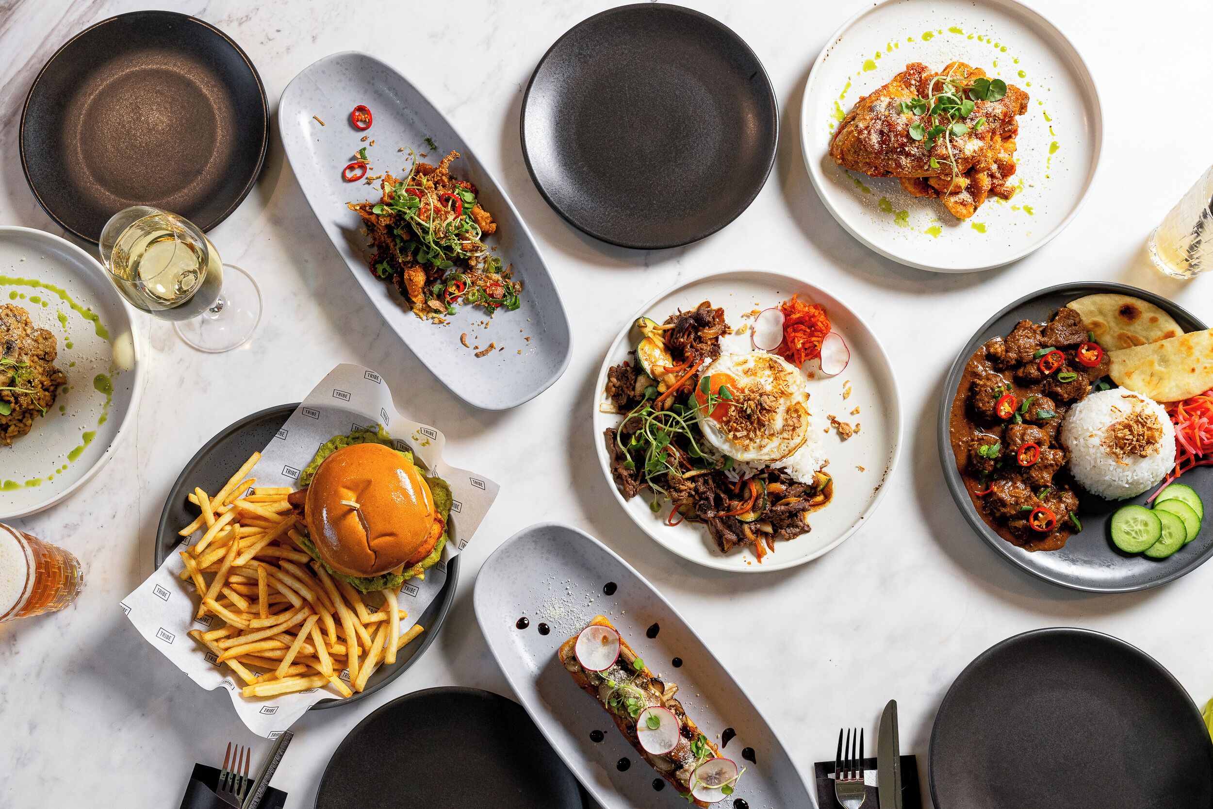 A variety of dishes on plates, a burger, and a glass of beer on a table.