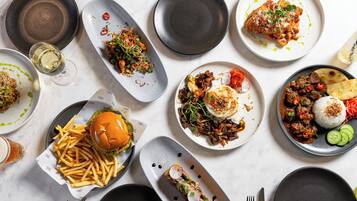 A variety of dishes on plates, a burger, and a glass of beer on a table.