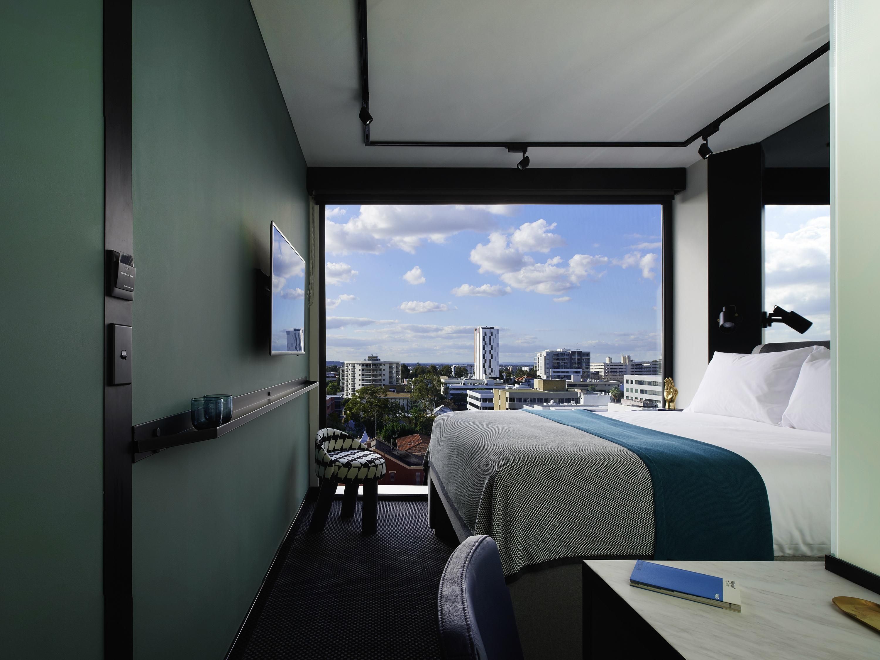 A hotel room with a large bed, a desk, a chair, and a view of the cityscape.