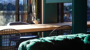 Una habitación moderna con una mesa de madera, dos sillas metálicas y un banco tapizado en verde.