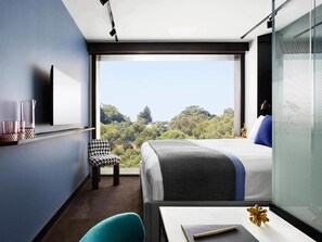 A modern hotel room with a large bed, a desk, a chair, and a view of a forested area. - Tribe Perth Kings Park (West Perth)