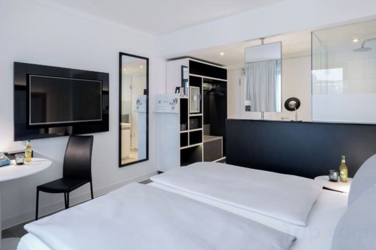 A modern hotel room with a bed, a desk, a chair, a TV, a wardrobe, and a mirror.