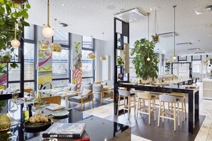 A modern restaurant with a central island, bar stools, and hanging plants. - INNSiDE by Meliá Hamburg Hafen (Hamburg)