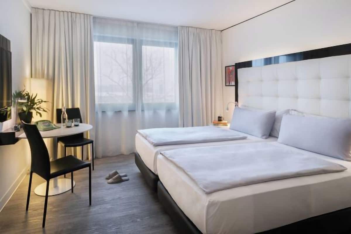 Ein Hotelzimmer mit Bett, Schreibtisch, Stuhl, Fenster mit Vorhängen und einer Pflanze.