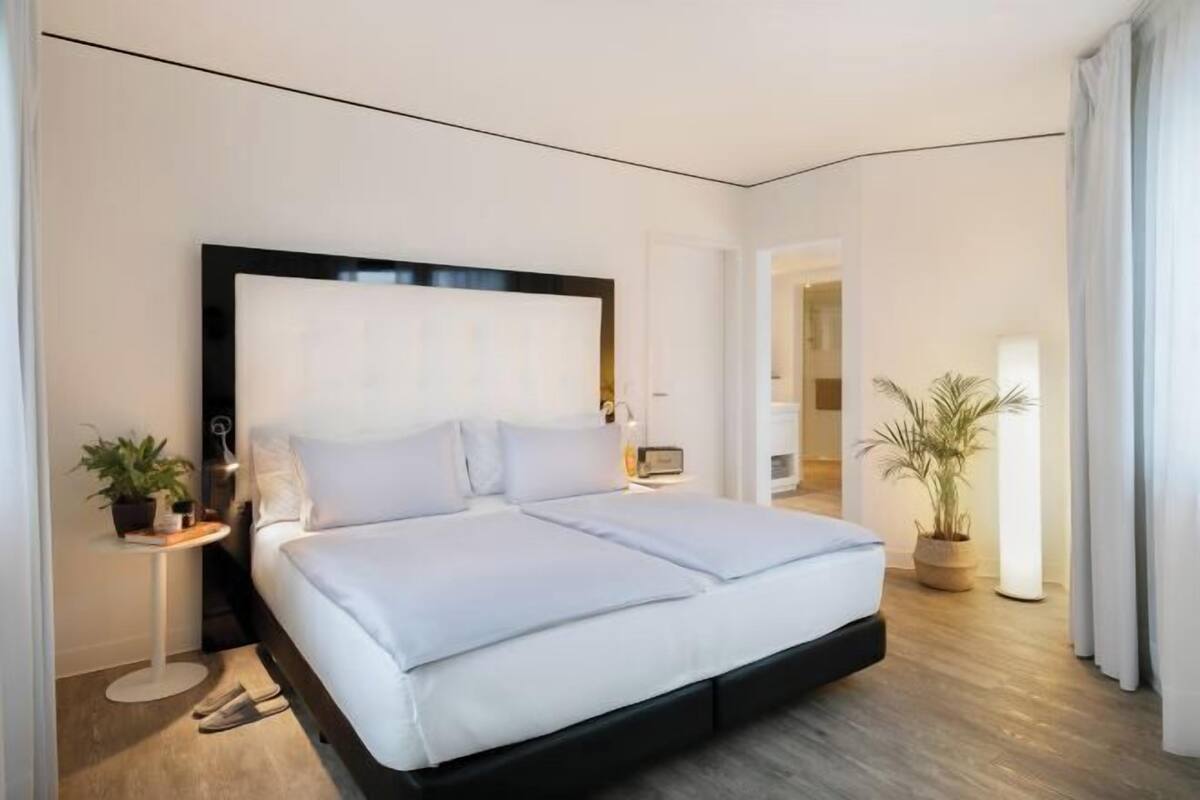 Ein modernes Hotelzimmer mit einem großen Bett, Nachttischen, einer Stehlampe und Blick auf den Flur.