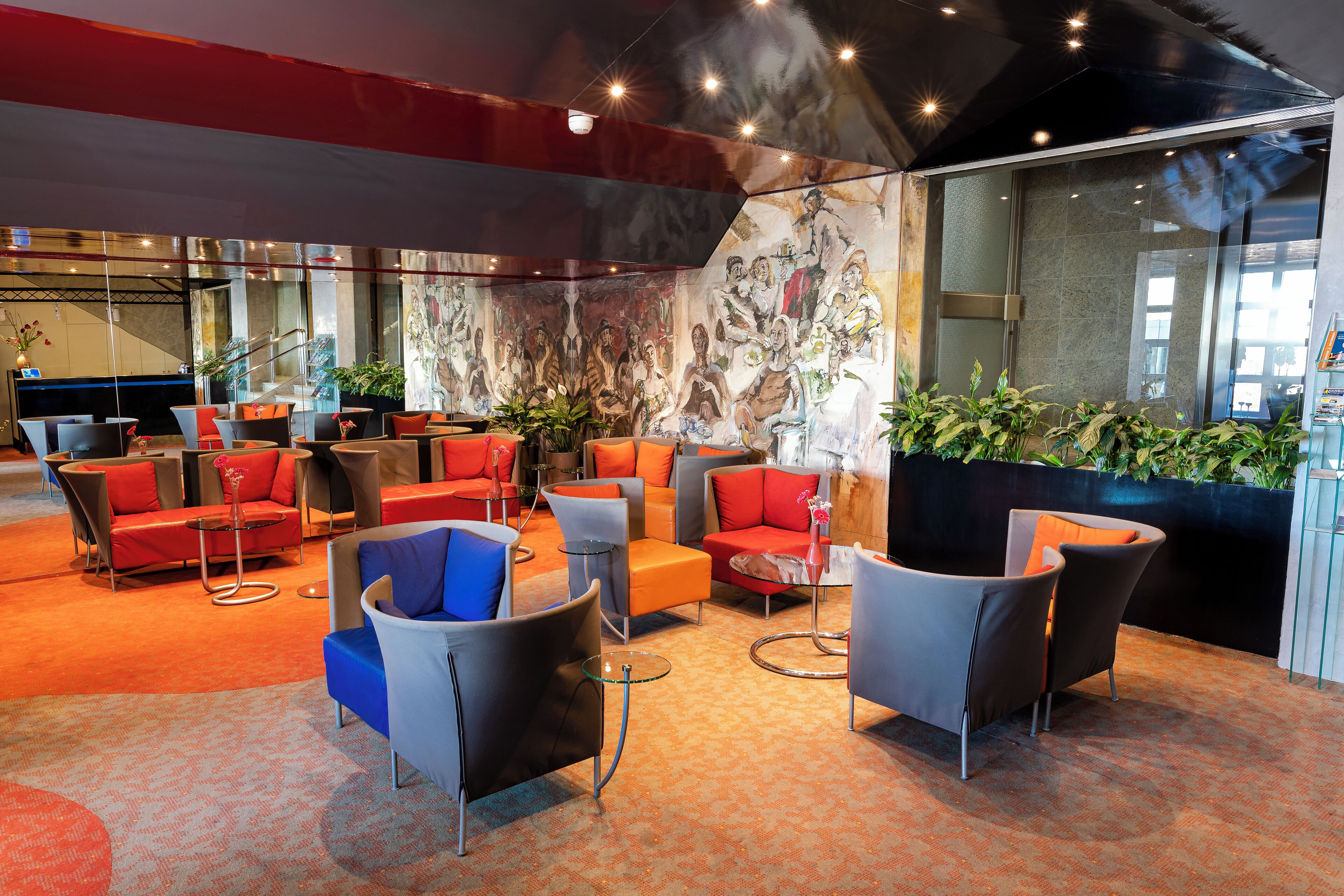 A modern lounge area with comfortable seating, a large mural, and a staircase in the background.