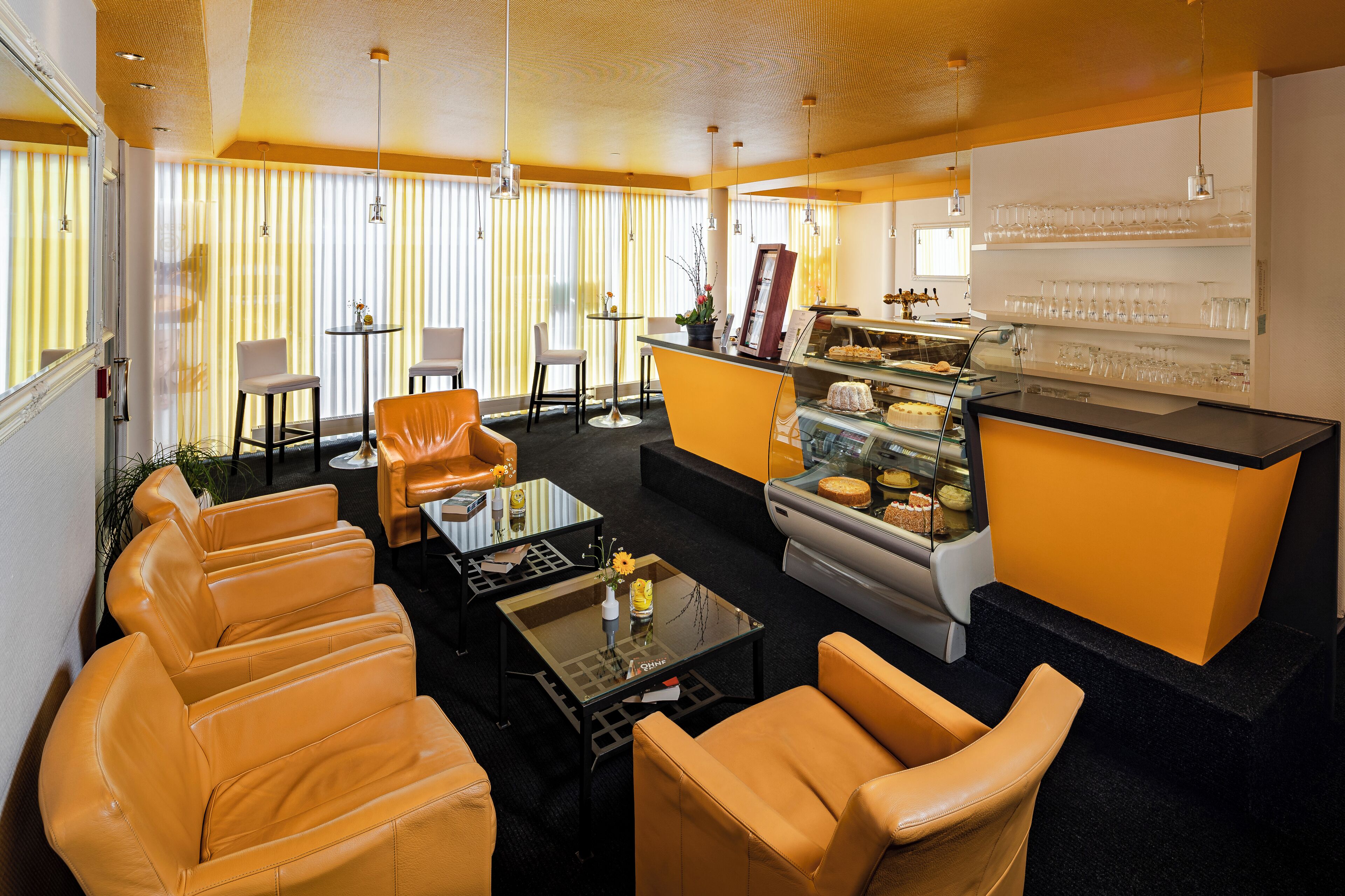 A modern hotel lobby with leather sofas, a coffee table, a small bar area with a display case, and a large window with vertical blinds.