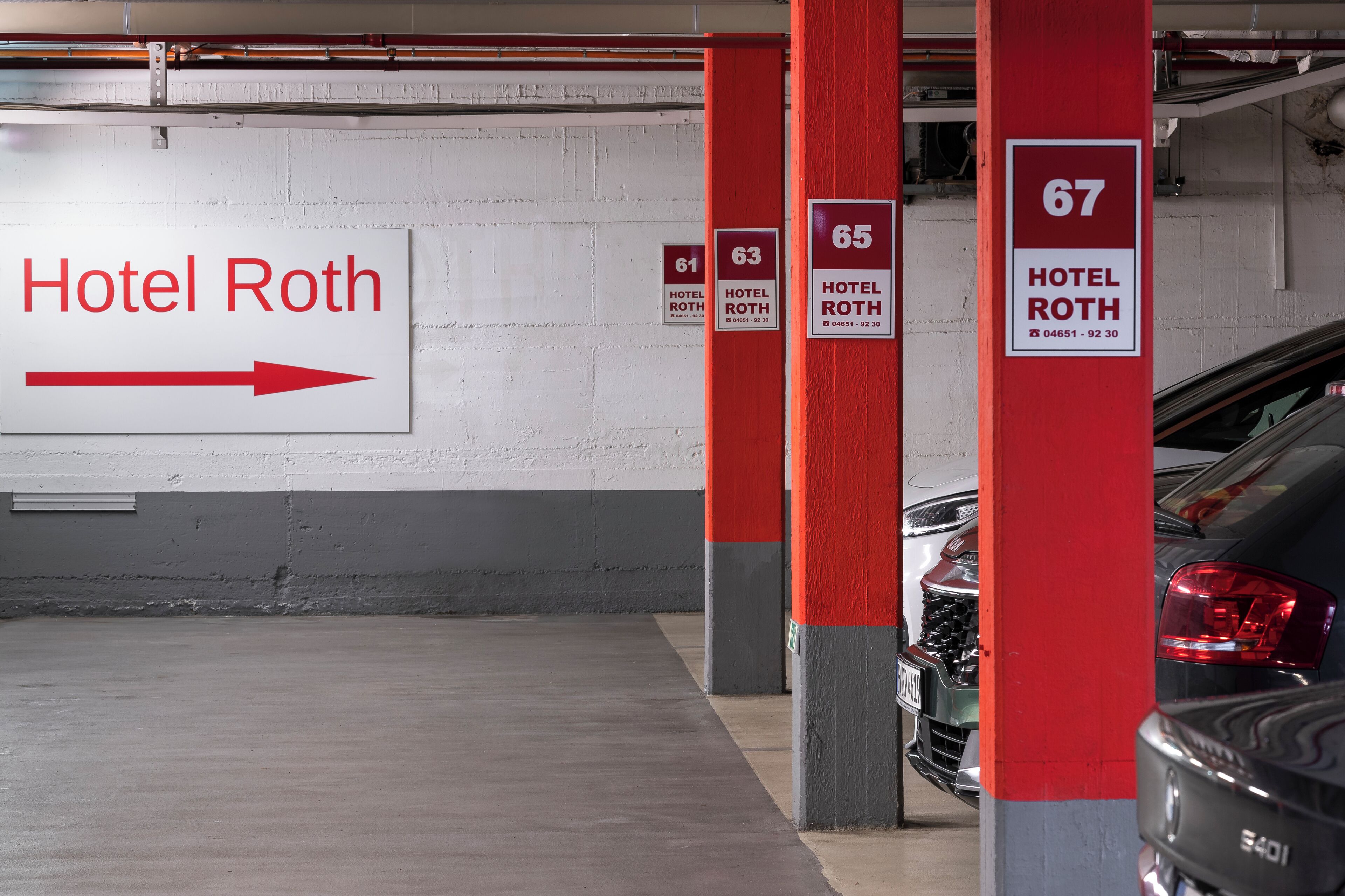 A parking garage with directional signs for Hotel Roth, including room numbers 61, 63, 65, and 67.