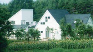 Two white houses with sloped roofs, surrounded by a forested area and a cornfield. - St village (Hokuto)