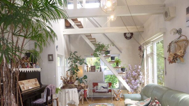 A spacious living room with a high ceiling, a staircase, and a variety of plants. - St village (Hokuto)