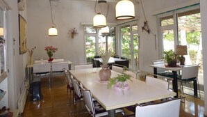 A spacious dining area with high ceilings, pendant lighting, and large windows offering views of greenery outside. - St village (Hokuto)