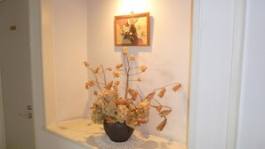 A hallway with a small display shelf containing a potted plant and a framed picture on the wall. - St village (Hokuto)