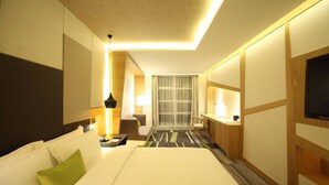 Ein Hotelzimmer mit einem großen Bett, einem Schreibtisch, einem Sessel, einem Fernseher und einem Fenster mit Vorhängen.