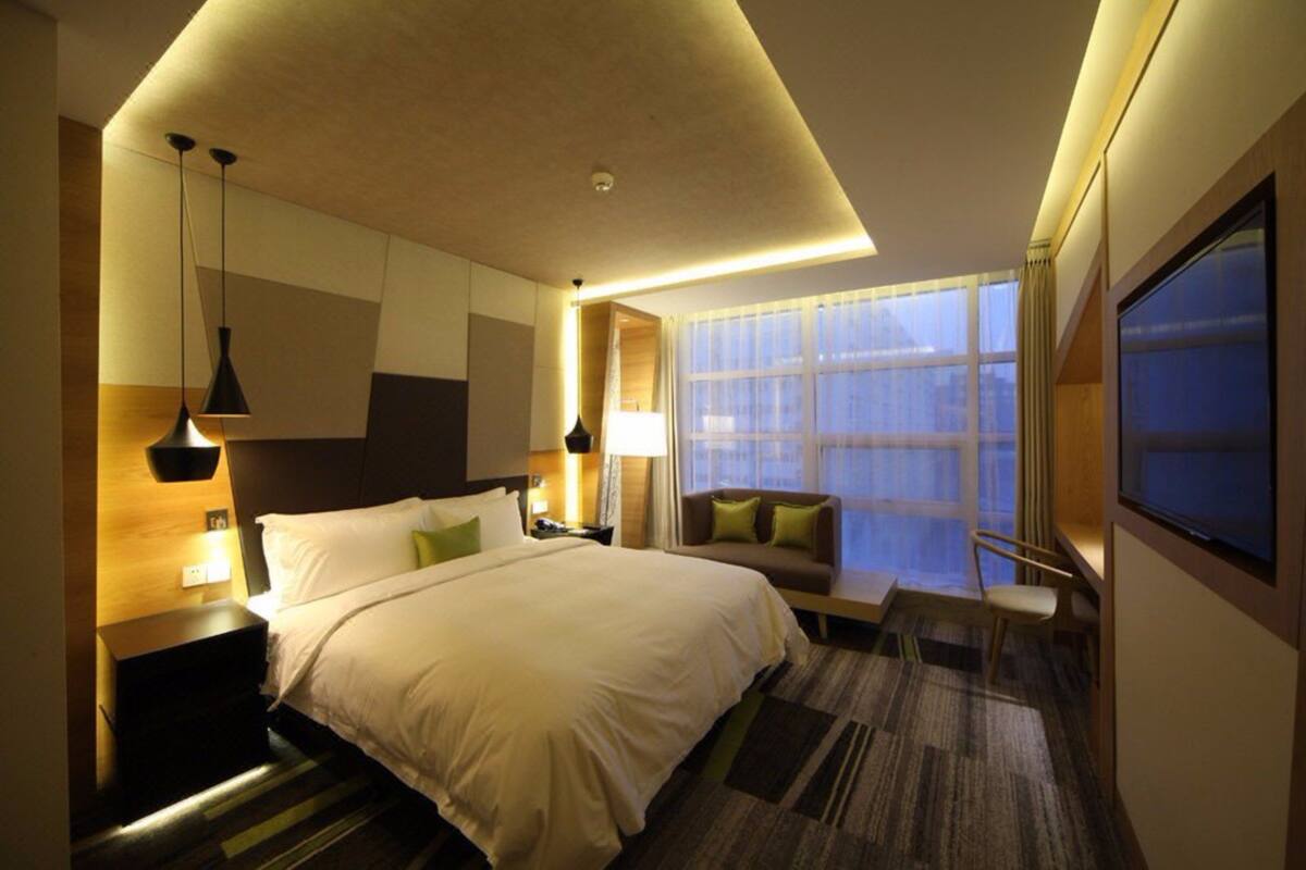 Une chambre d’hôtel avec un grand lit, un canapé, une télévision et une fenêtre avec des rideaux.