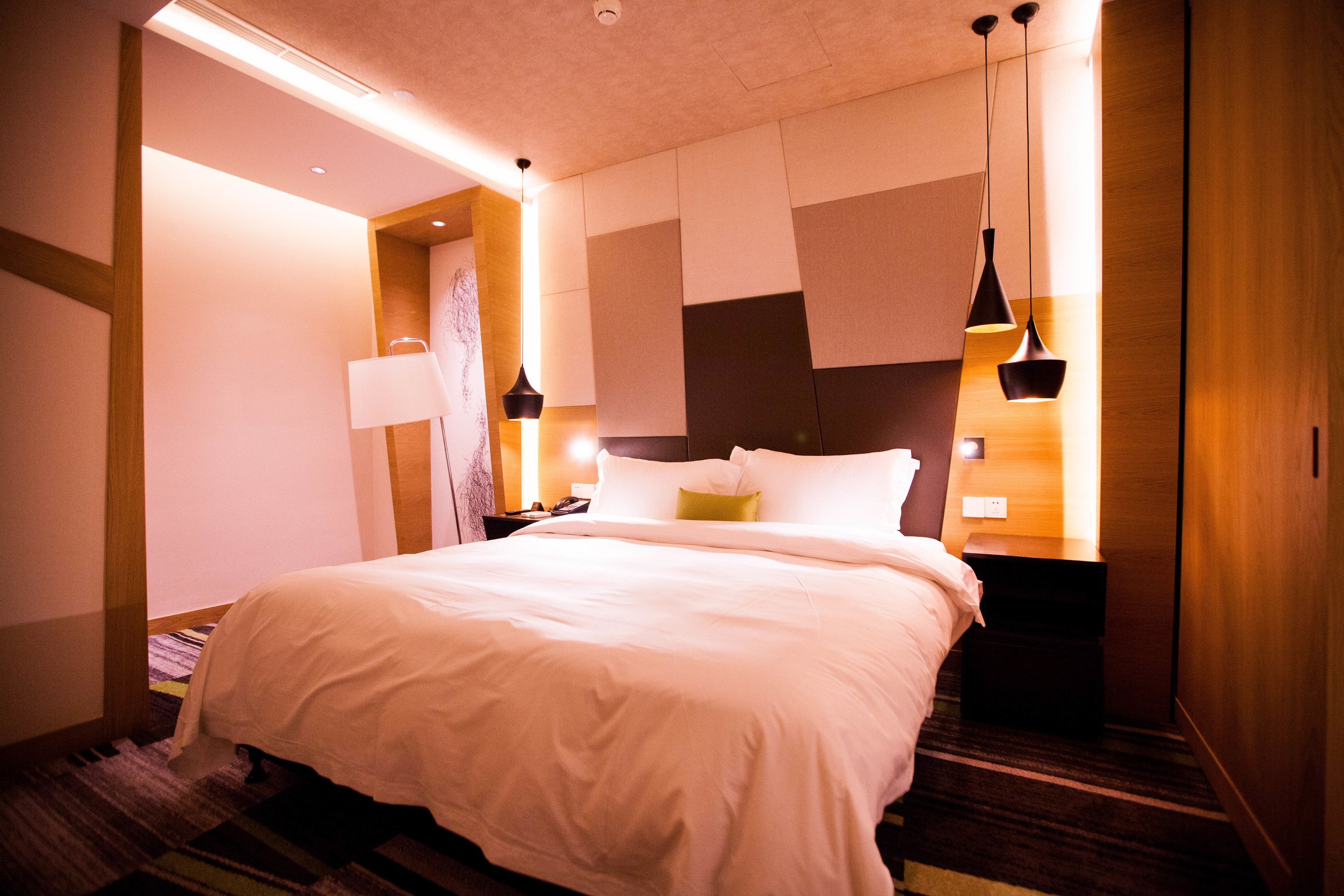 A modern hotel room with a large bed, bedside tables, and a unique wall design.