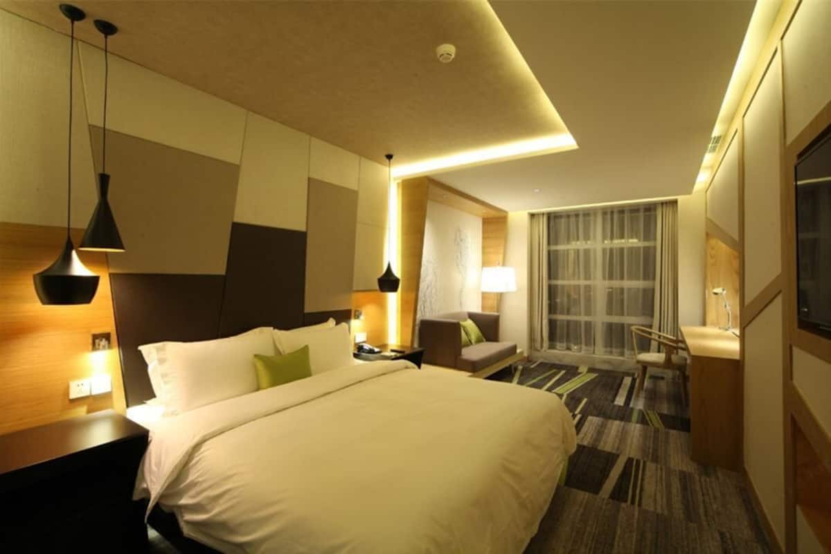 Une chambre d’hôtel avec un grand lit, des tables de chevet, un bureau, une chaise et une fenêtre avec des rideaux.