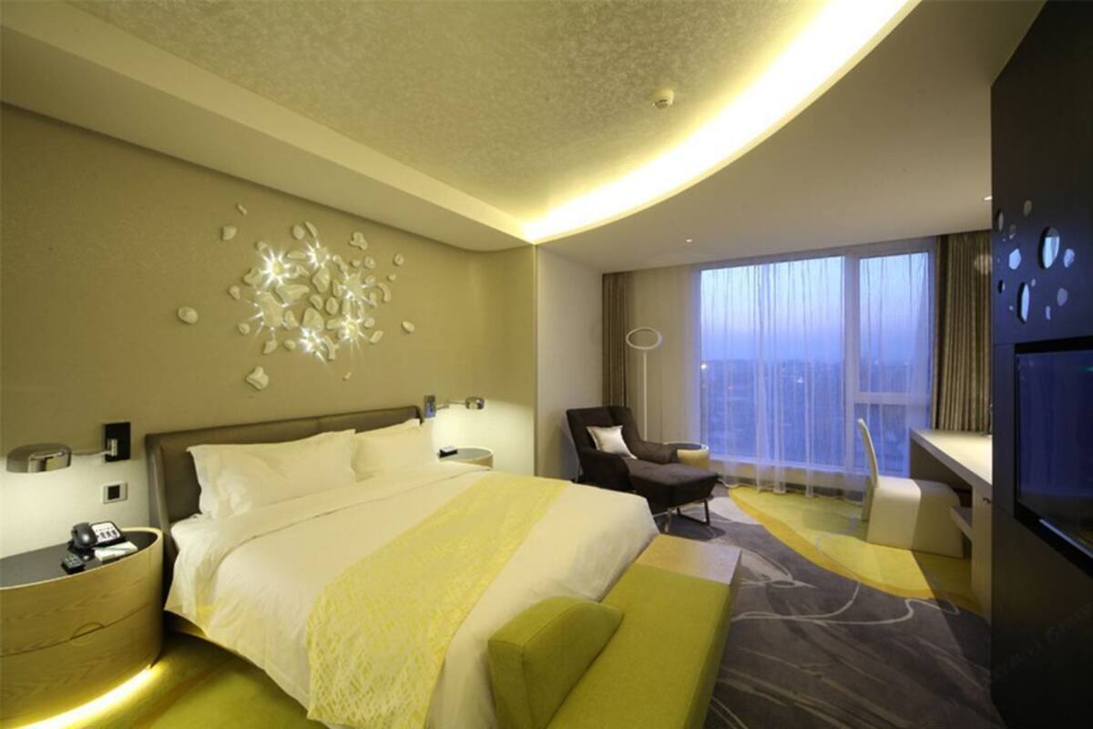Une chambre d’hôtel moderne dotée d’un grand lit, d’un coin salon, d’un bureau et offrant une vue sur la ville grâce à de grandes fenêtres.
