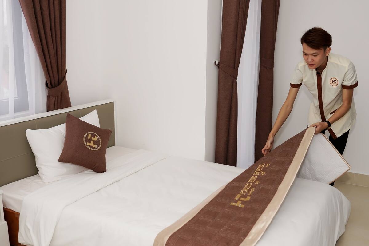 Una cama bien hecha con una colcha marrón y un almohadón con un logotipo.