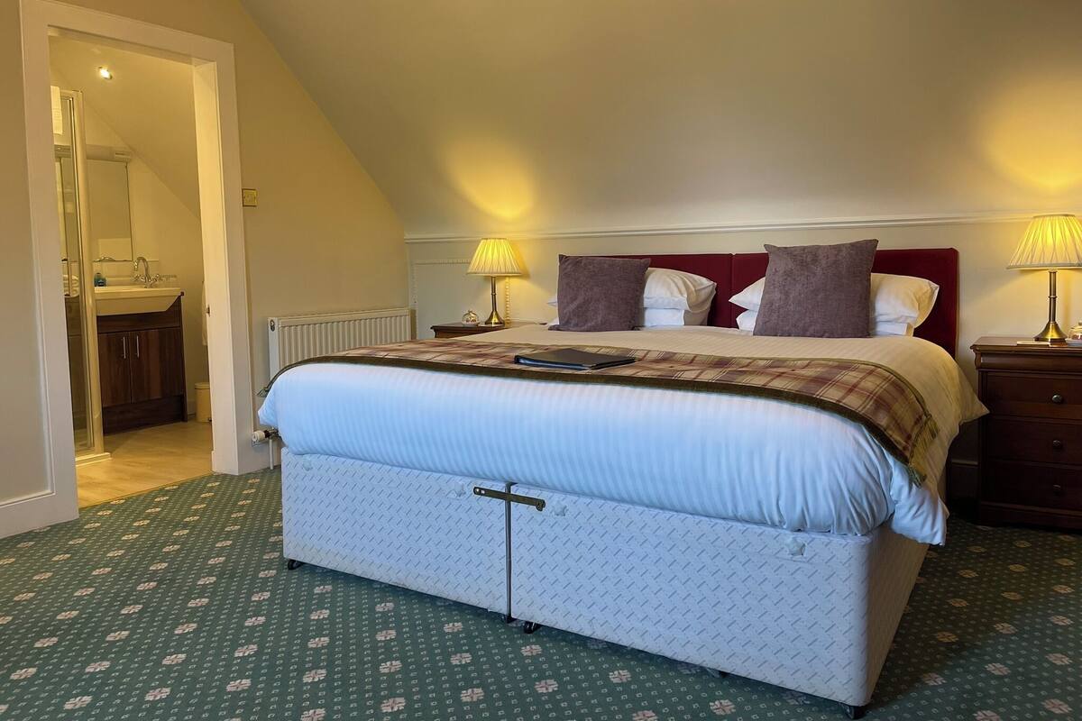 A bedroom with a bed, bedside tables, a lamp, and a bathroom visible through an open door.