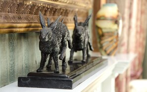 Deux sculptures d’animaux en bronze, posées sur un socle de marbre, se dressent devant un mur décoratif orné de motifs complexes.