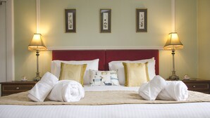 A neatly made bed with white linens, two pillows, and two rolled towels. There are two bedside tables with lamps, and three framed pictures on the wall above the bed. -  Ravenscourt Guest House (Grantown-on-Spey)