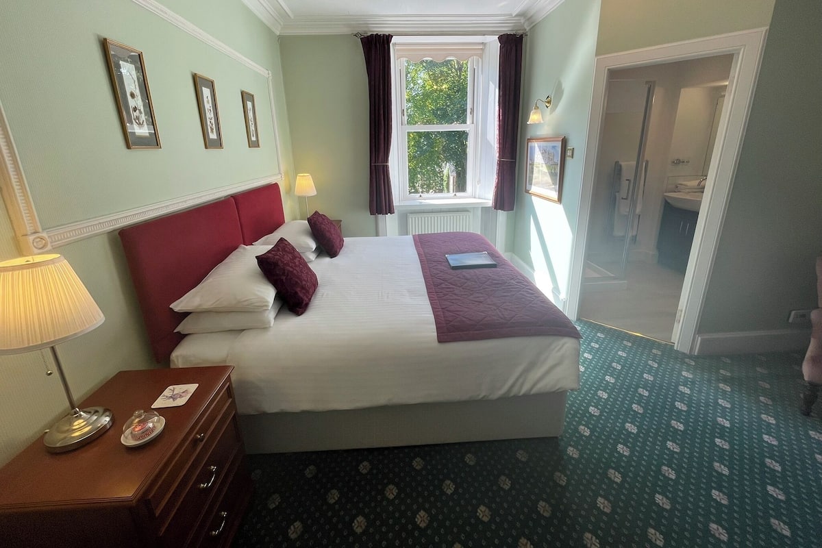 A hotel room with a large bed, a nightstand, a lamp, and a window with curtains.