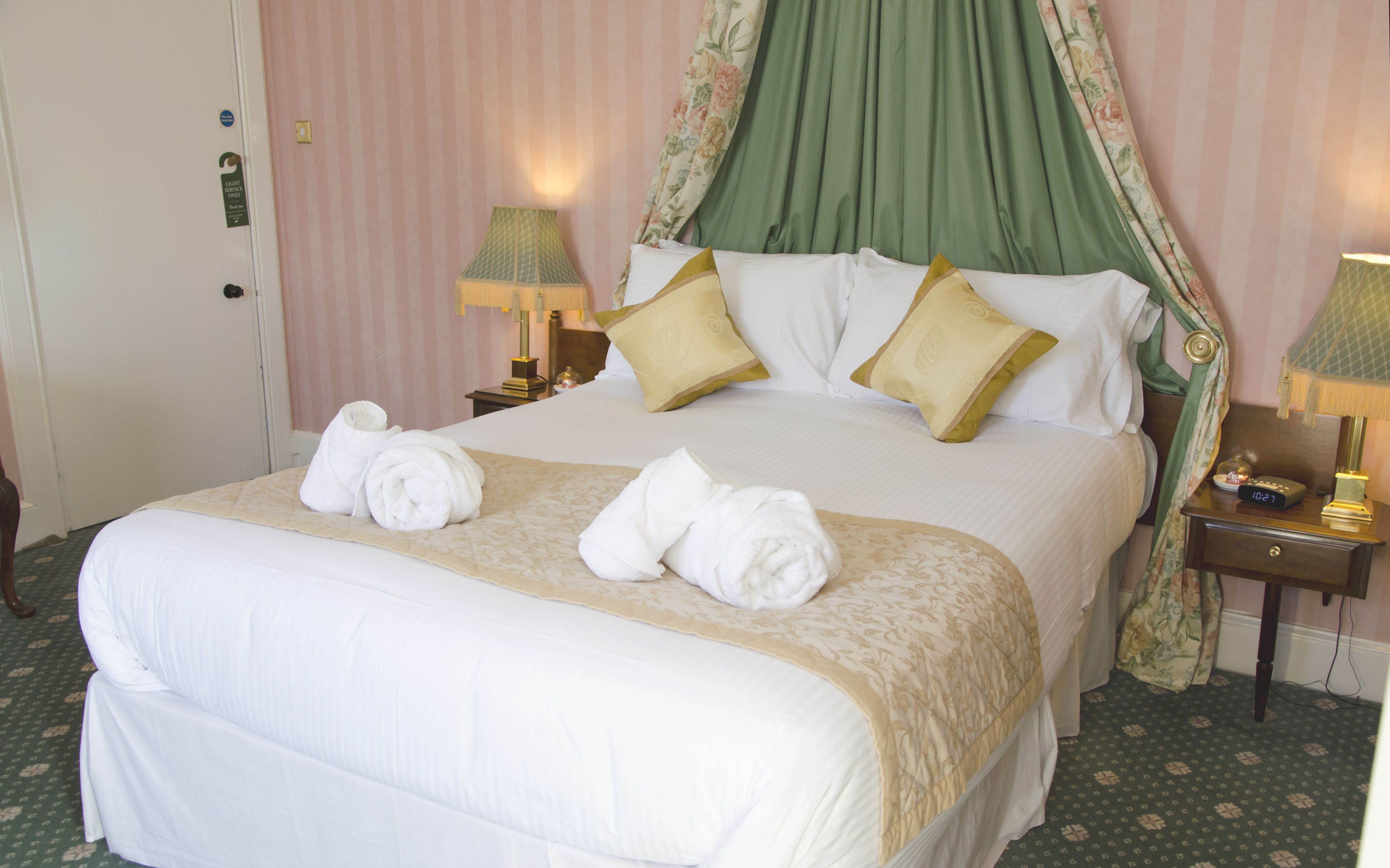 A neatly made bed with a canopy, two bedside lamps, and a clock on the nightstand.