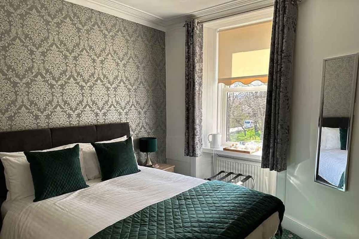A hotel room with a large bed, a window with curtains, a radiator, and a mirror on the wall.