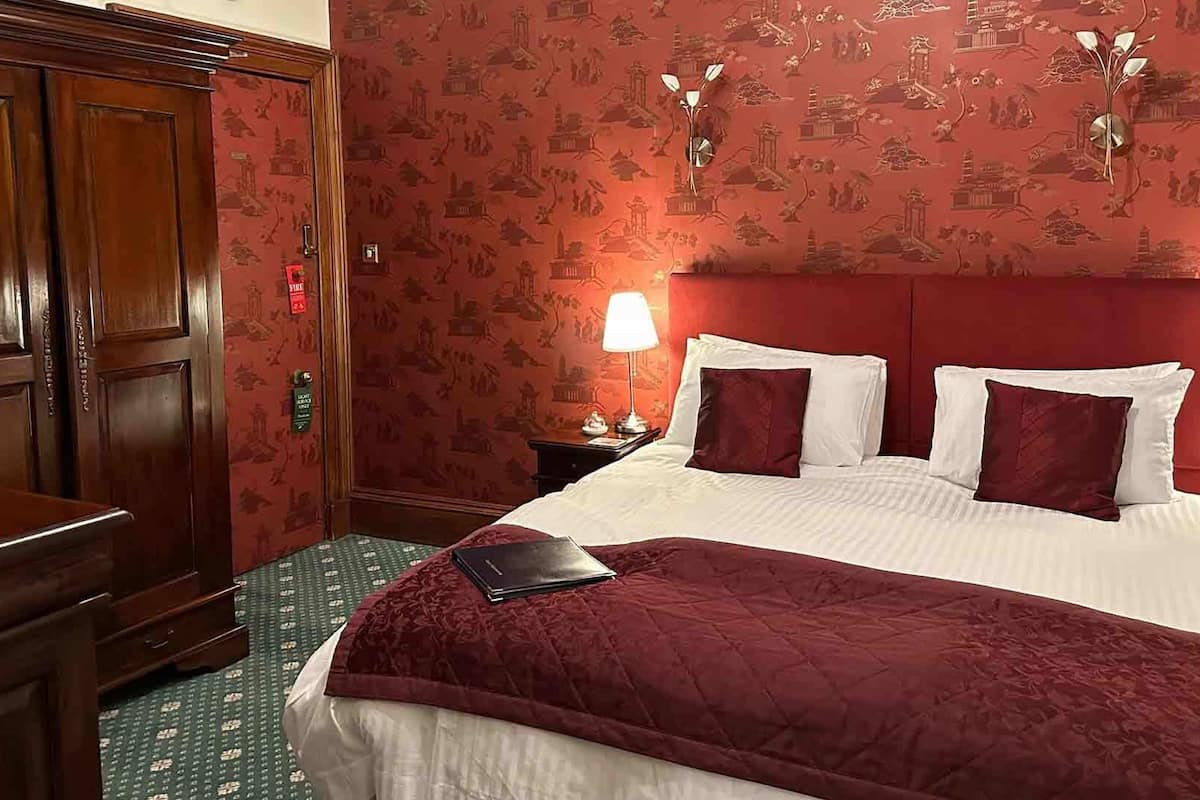 A hotel room with a large bed, two bedside lamps, a wooden wardrobe, and a green patterned carpet.