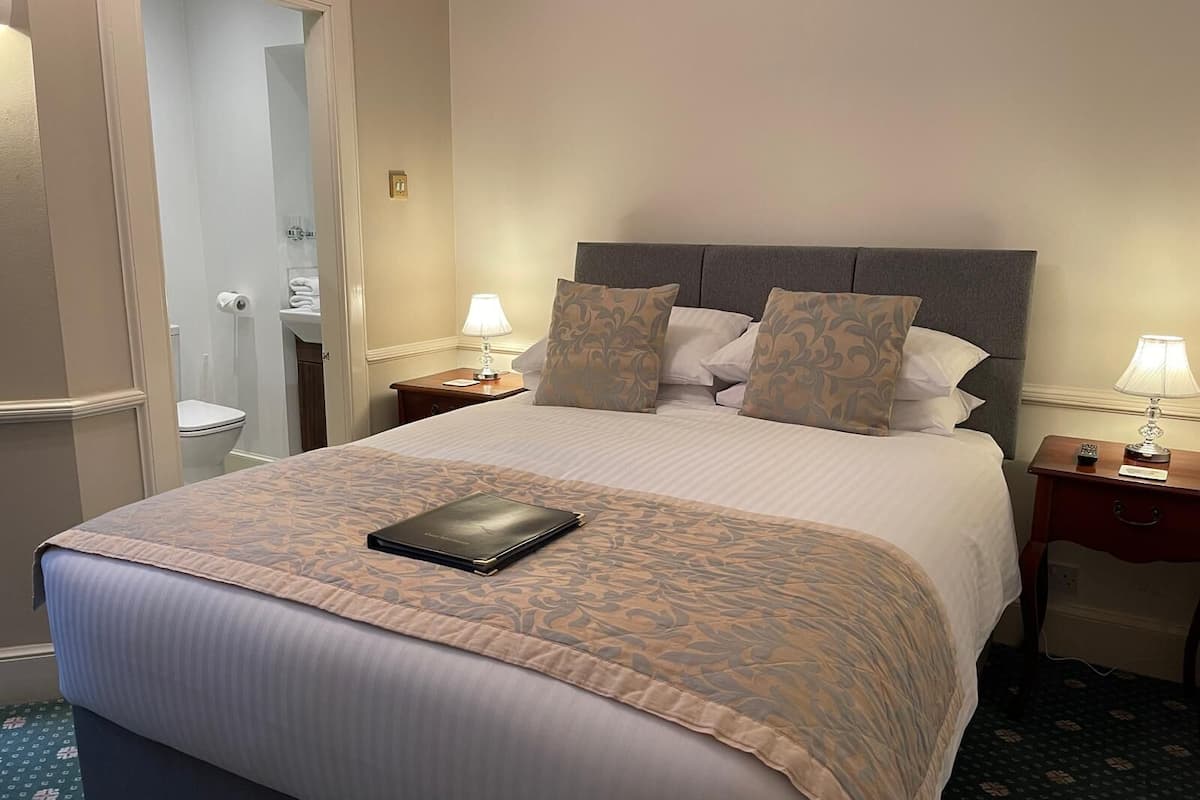A neatly made bed with a patterned bedspread, two bedside lamps, and a nightstand with a remote control.