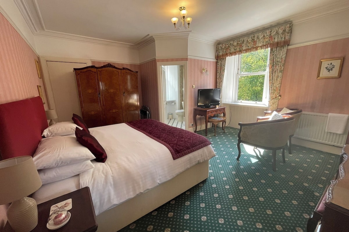 A hotel room with a large bed, a desk with a TV, a chair, and a window with curtains.