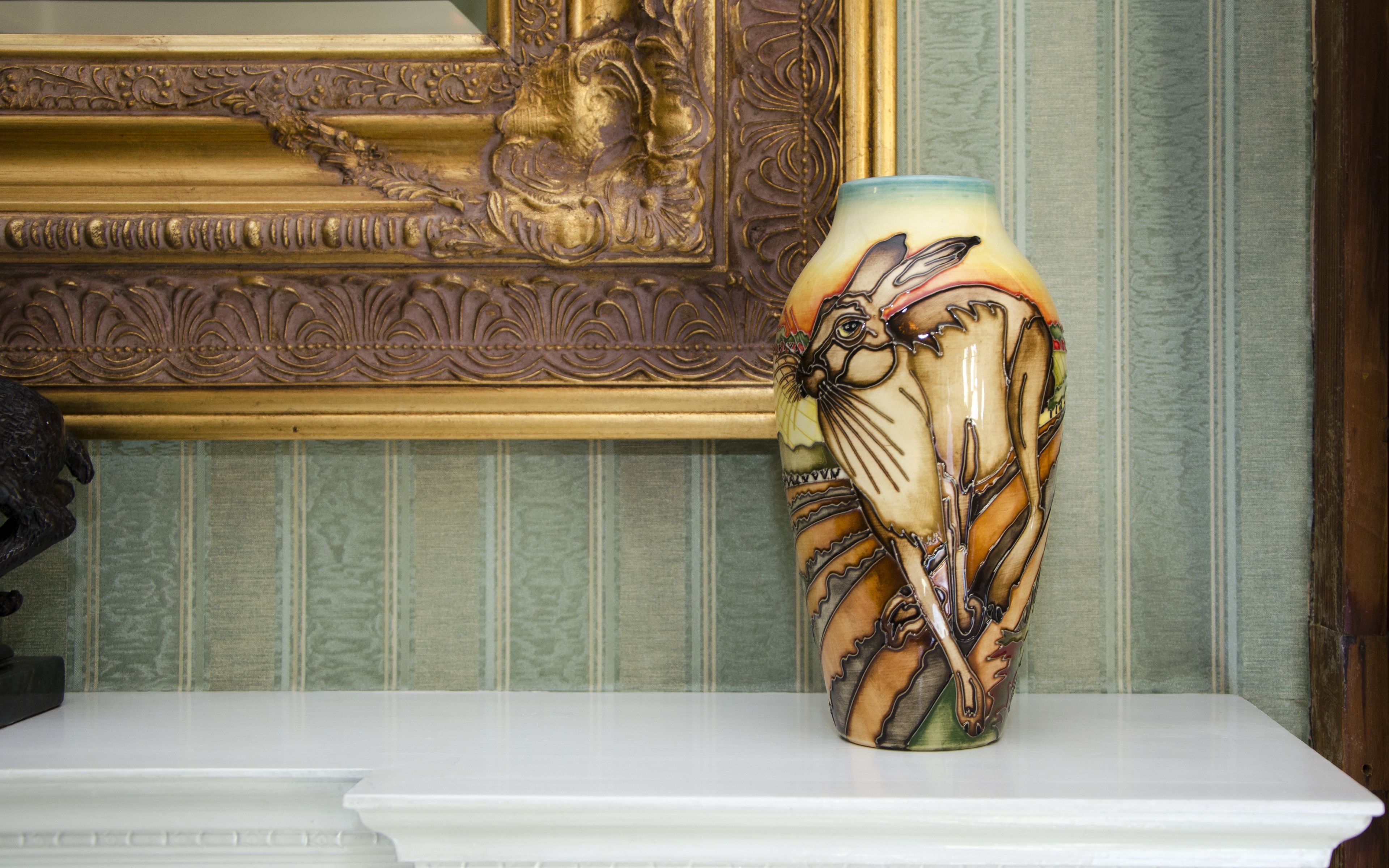 A vase with a floral design on a white shelf.