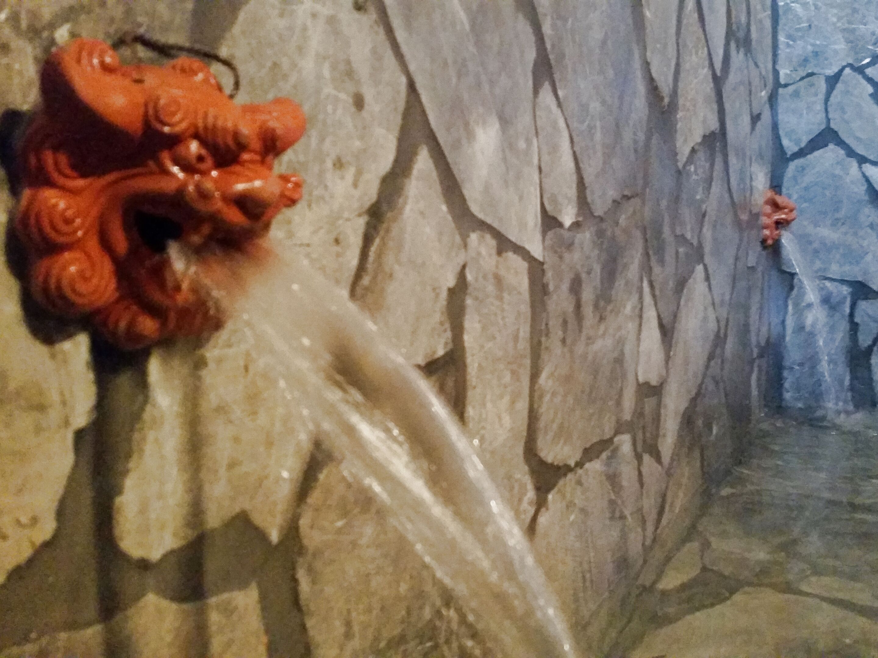 A stone wall with a red, ornate water spout.