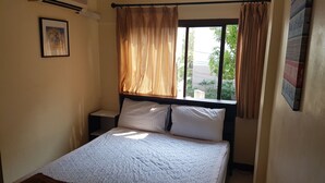 A bedroom with a bed, a window with curtains, a nightstand, and a wall-mounted air conditioning unit. - Sandman hotel and Sports bar (Pattaya)