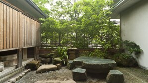 Un jardín japonés tradicional con una terraza de madera, asientos de piedra y una gran variedad de plantas.