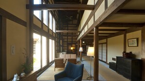 Un interior japonés tradicional con suelo de tatami, un sillón azul, vigas de madera y vistas a través de amplios ventanales.