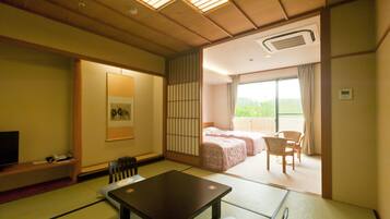 A traditional Japanese room with tatami flooring, a low table, a TV, and a bed with a view of greenery outside.