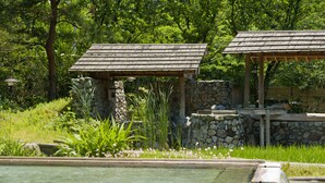 Una estructura de piedra con techo de madera, rodeada de abundante vegetación y un área pequeña con piscina.
