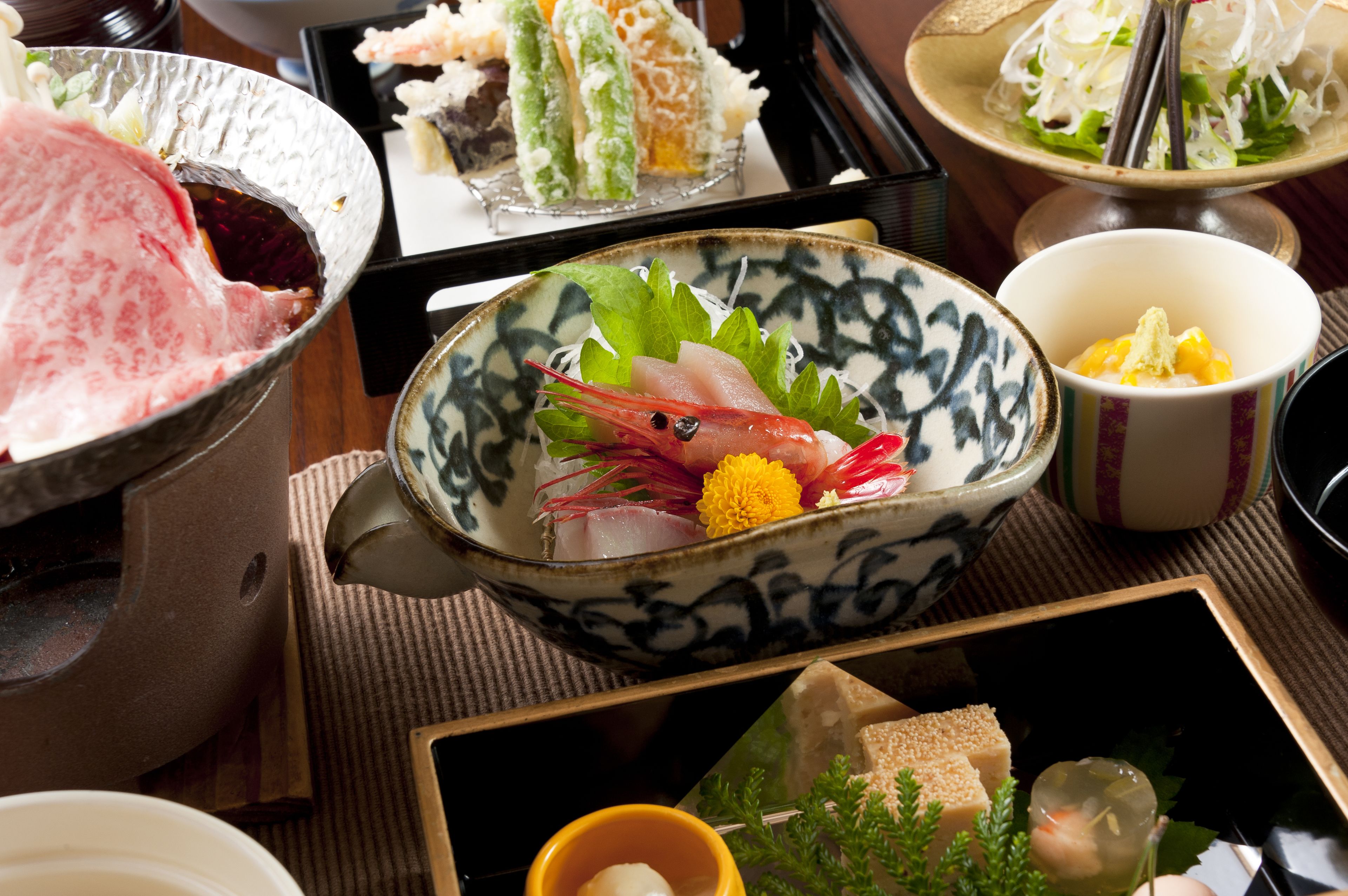 A variety of dishes including sashimi, vegetables, and tofu, arranged on a table with a traditional Japanese aesthetic.