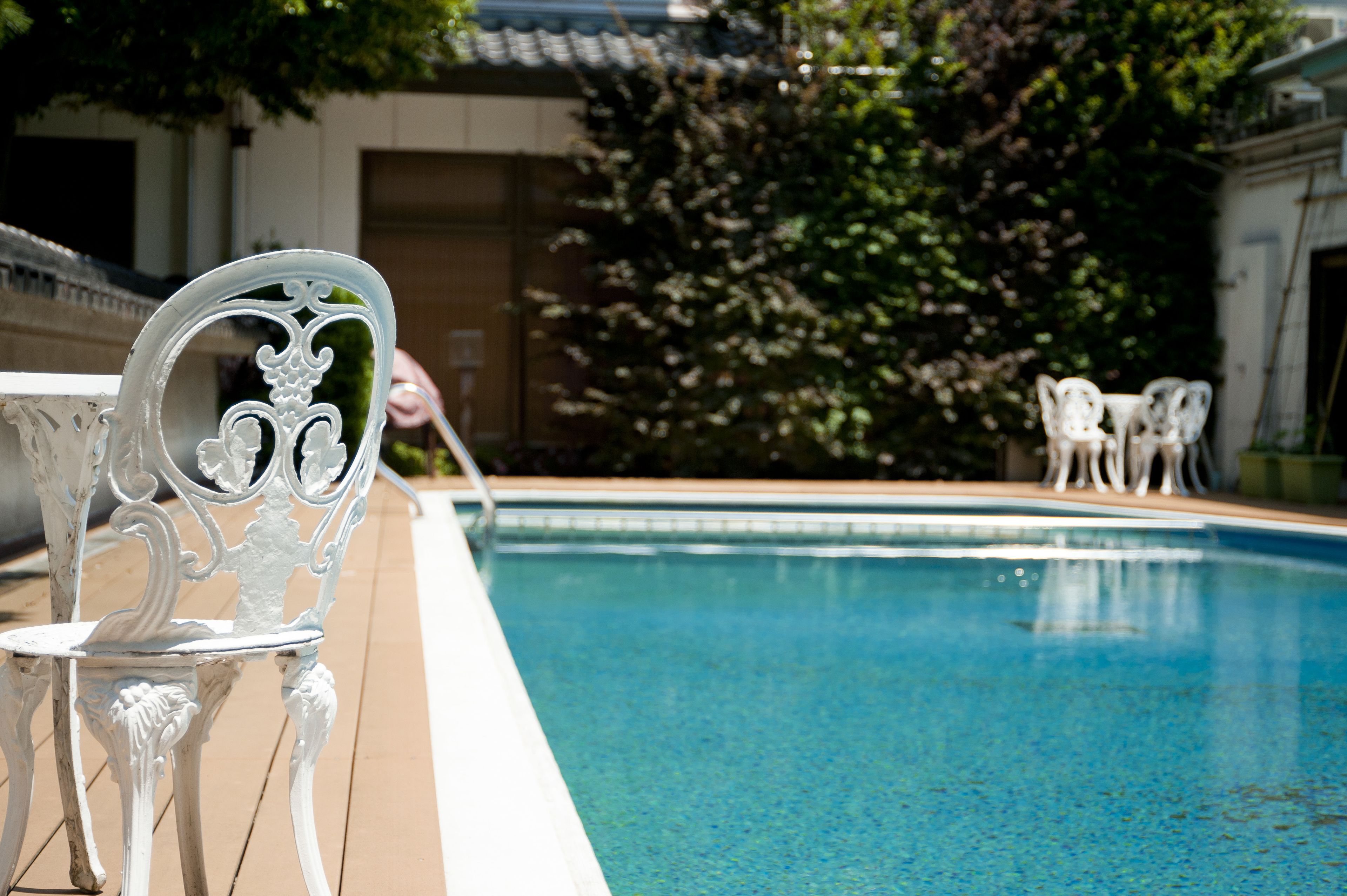 A swimming pool with white metal chairs and a table on the deck.