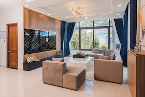 A modern living room with a large window, a wooden accent wall, and a chandelier. - Tea Resort Dalat by Doi Dep (Da Lat)