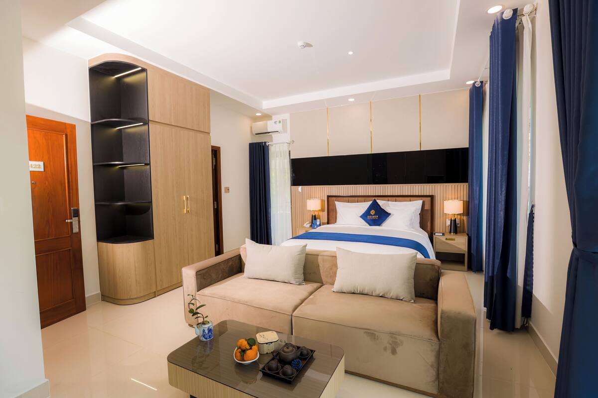 A hotel room with a bed, a sofa, a coffee table with a teapot and fruit, and a wardrobe.